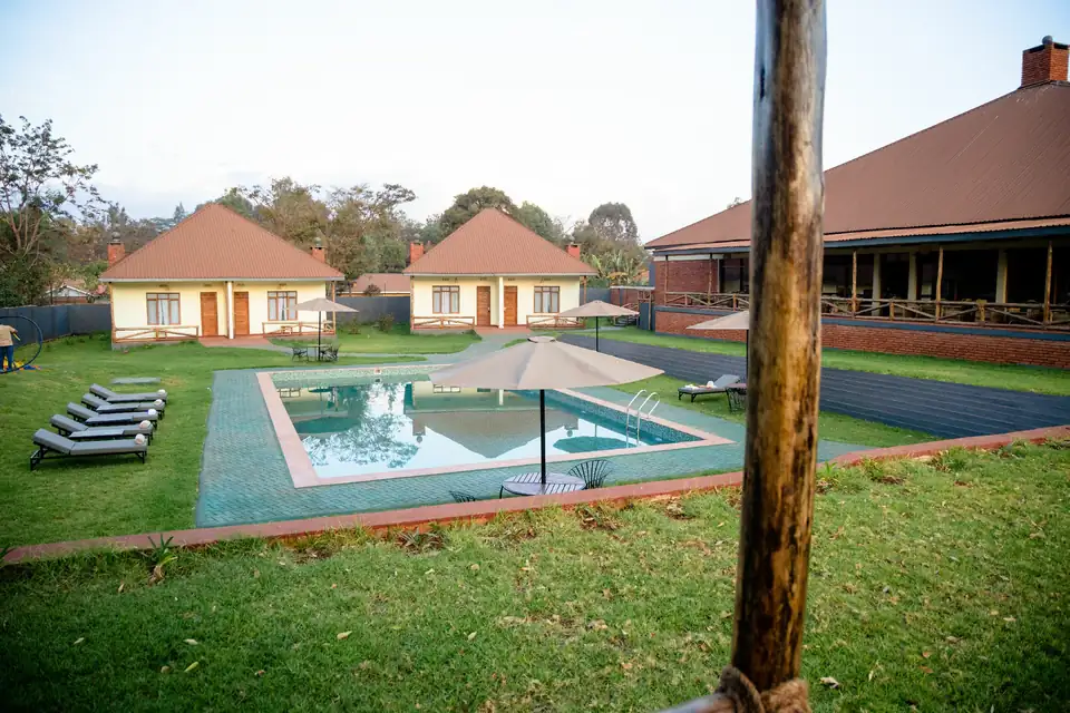 Two villas with hipped roofs behind the swimming pool and lawn at Karatu Villas Lodge