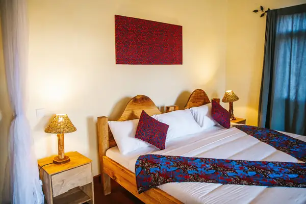 Single room with a carved wooden bed and kitenge throw